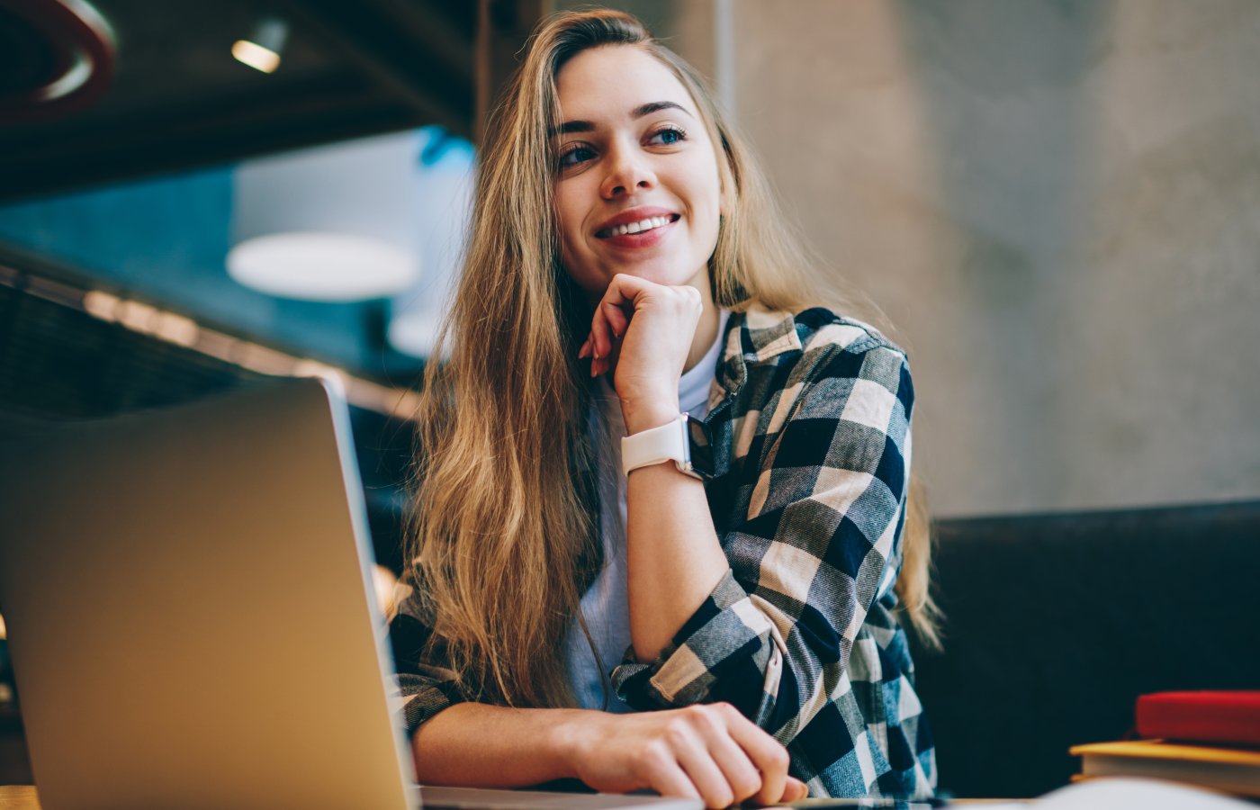 Young woman looking up and smiling while working on laptop.
