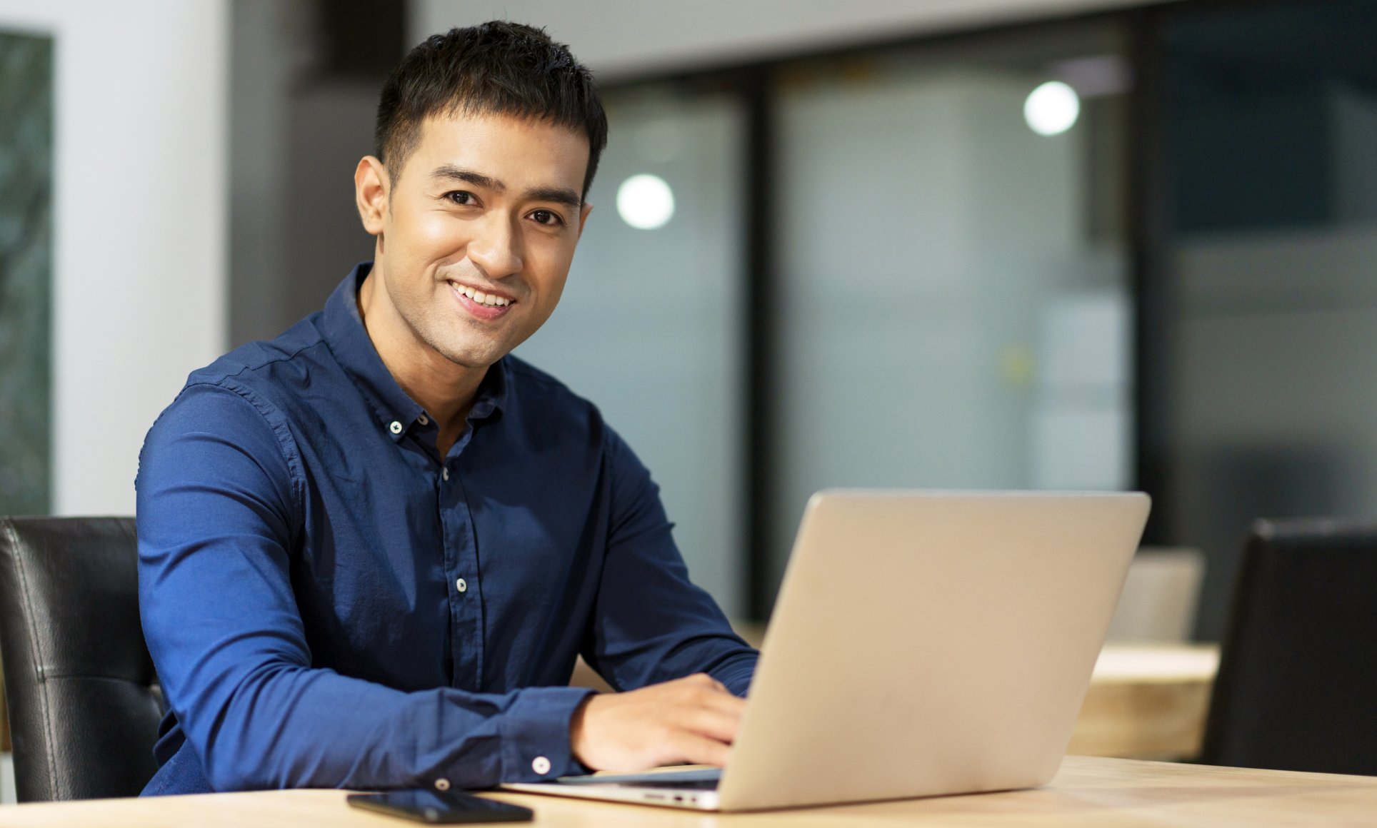man working at a laptop looking up and smiling